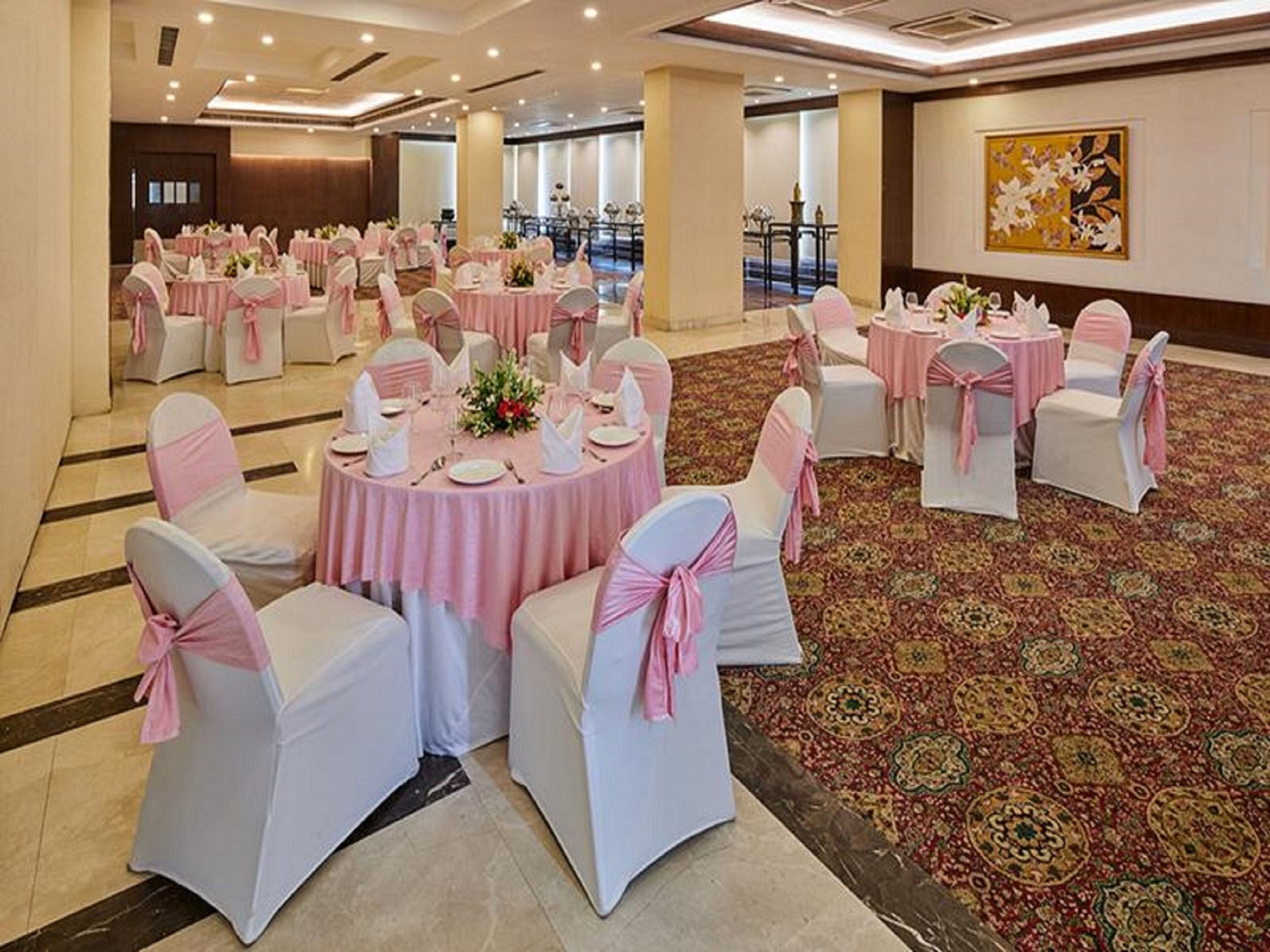 A banquet hall with round tables, white chairs with pink sashes, and a patterned carpet.