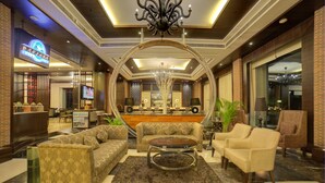 A spacious lobby with a reception desk, sofas, armchairs, and a chandelier. - Goldfinch Hotel Delhi NCR (Faridabad)