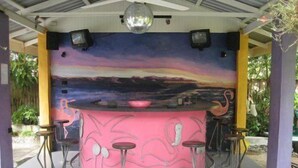 A pink bar with a mural of a sunset, surrounded by stools and a disco ball. - Pink Flamingo Resort (Port Douglas)