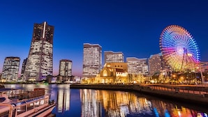 A city skyline with modern skyscrapers and a brightly lit Ferris wheel reflecting on the water.