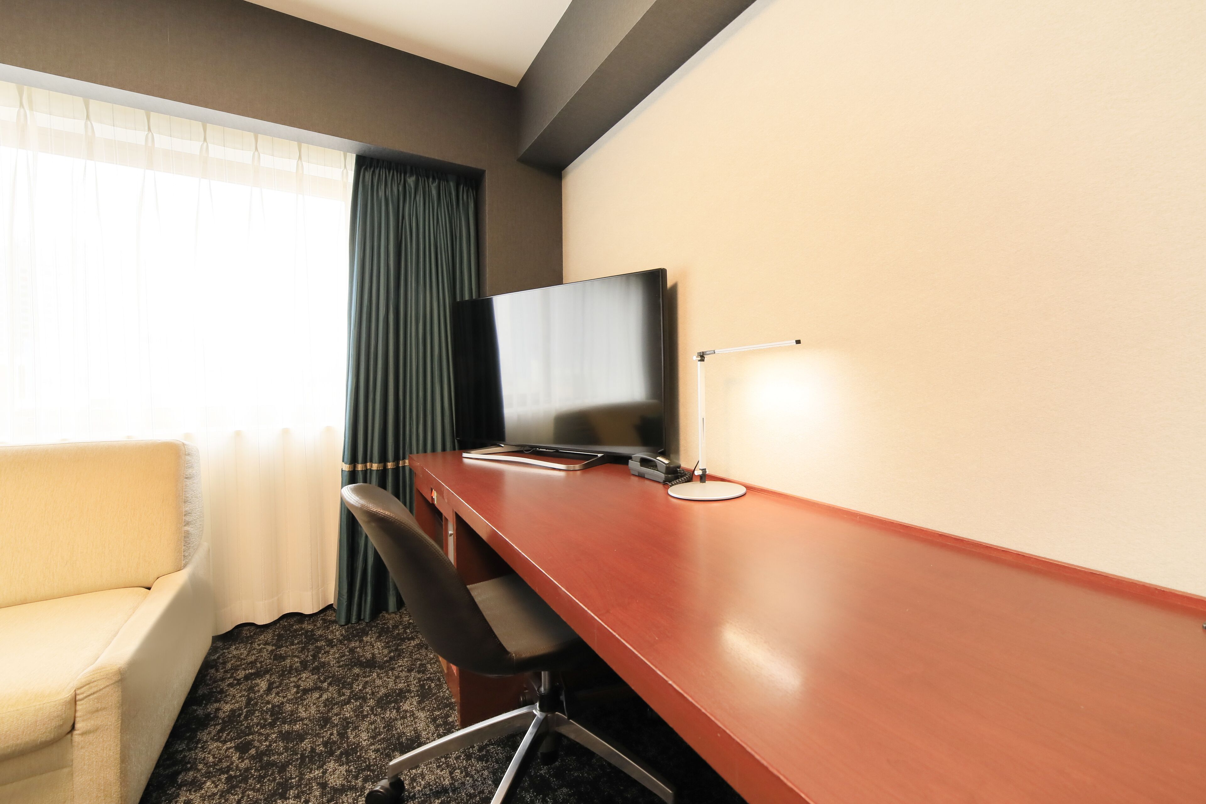 A hotel room with a wooden desk, a television, a chair, and a sofa.