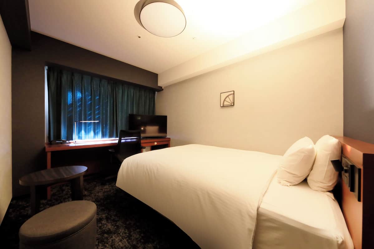 A hotel room with a bed, a desk, a chair, a television, and a small table.