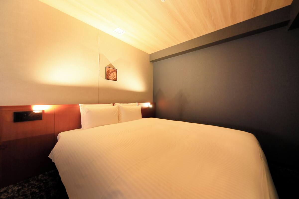 A hotel room with a large bed, wooden headboard, and a wall-mounted picture.