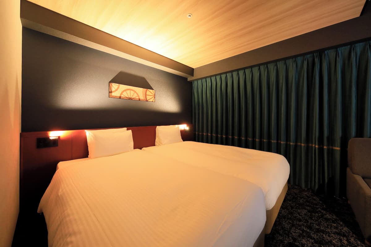A hotel room with a large bed, a headboard with lights, a wall-mounted artwork, and a curtain.