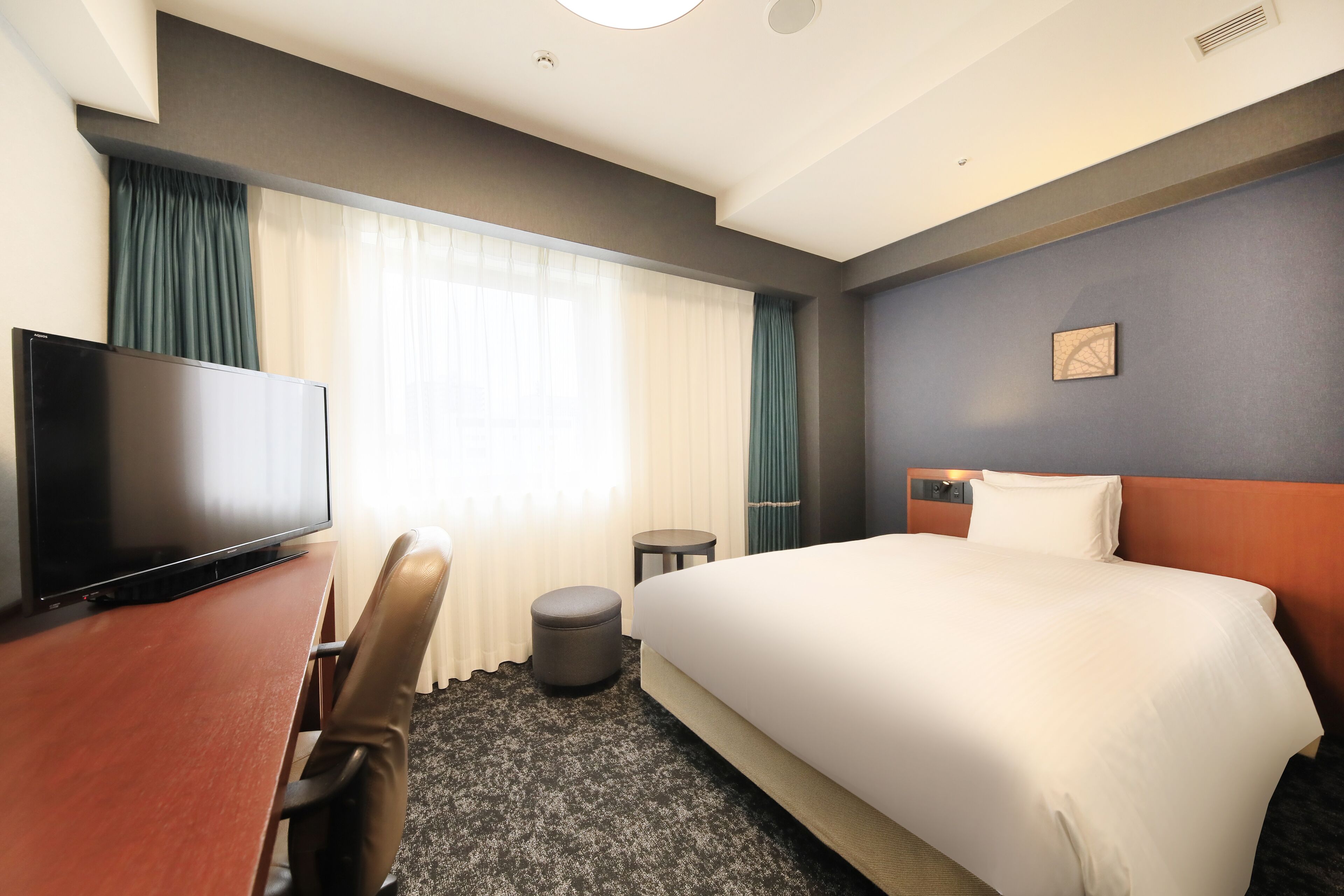 A hotel room with a bed, a desk, a television, and a small round table.