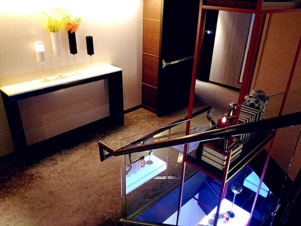 A modern hotel lobby with a glass railing, a reception desk, and a staircase.