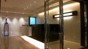 Un hall d’hôtel moderne avec des cloisons en verre, un comptoir d’accueil et un écran de télévision.
