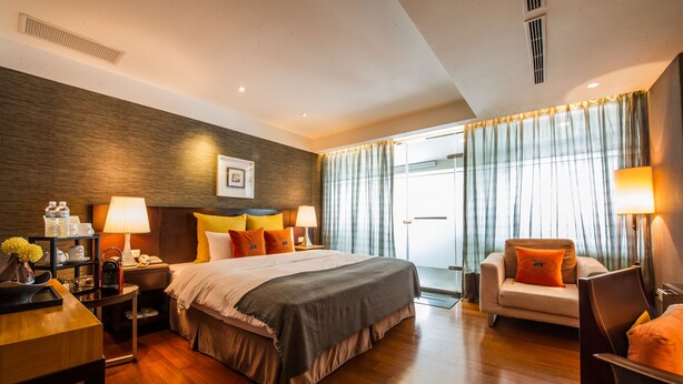 Une chambre d’hôtel avec un grand lit, des tables de chevet, un bureau, une chaise et une vue sur l’extérieur à travers des rideaux.