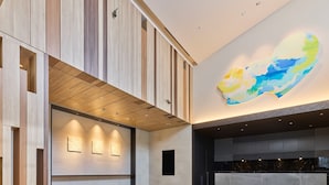Un moderno vestíbulo con mostrador de recepción, paneles de madera y un gran mural abstracto en el techo.
