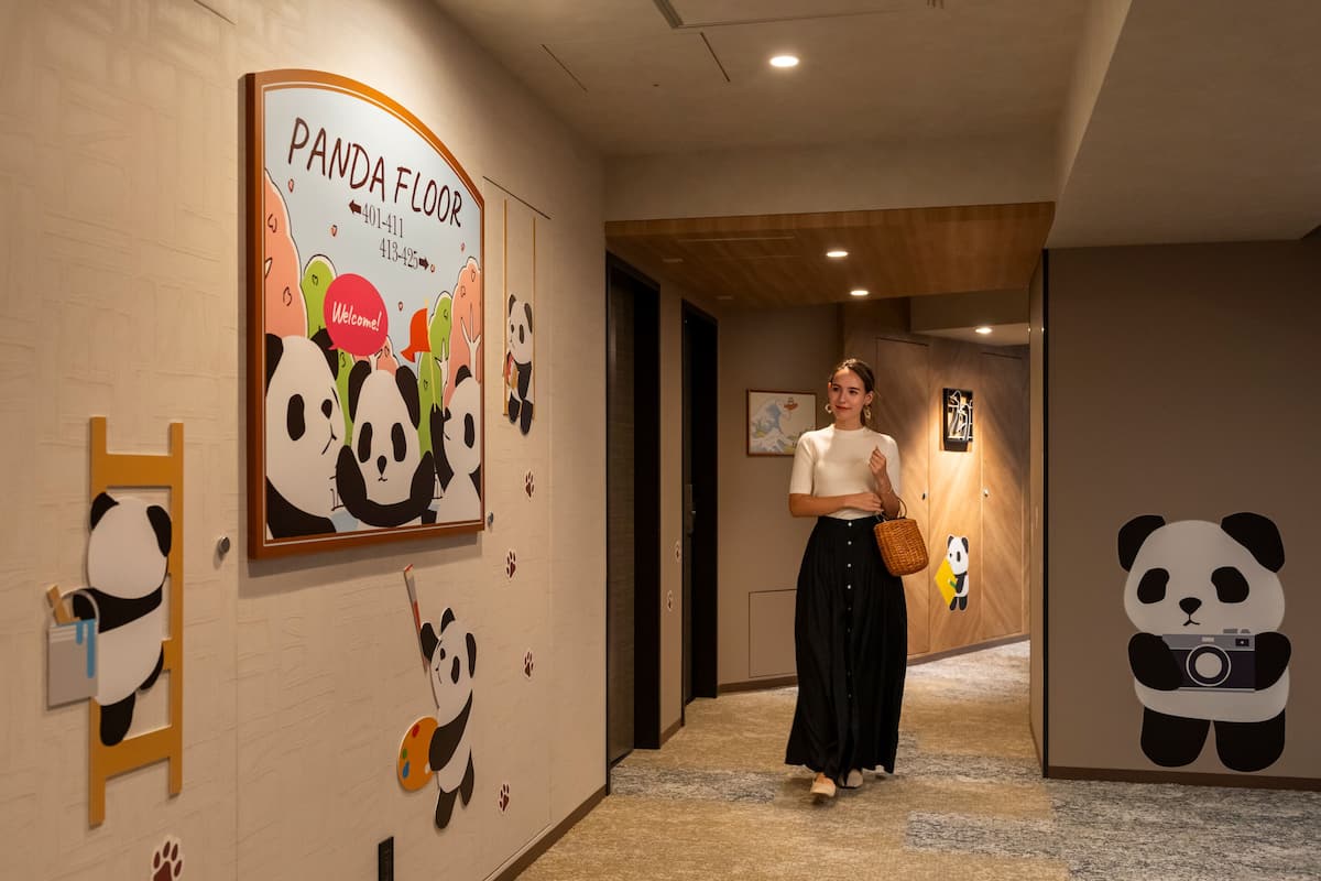Um corredor com decoração temática de panda, incluindo uma placa para o Andar do Panda, uma figura de panda na parede e um panda com uma câmera.