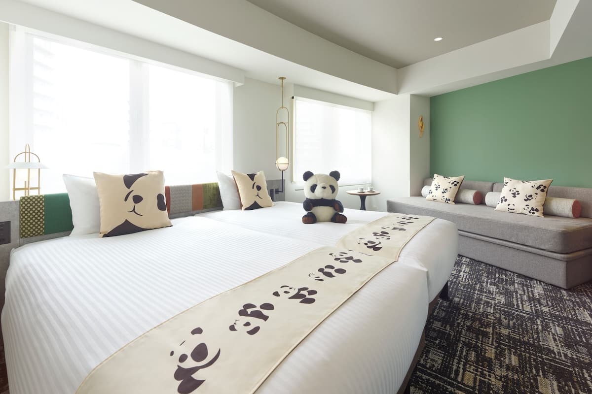 Quarto de hotel com uma cama grande, um sofá e um bichinho de pelúcia de panda.