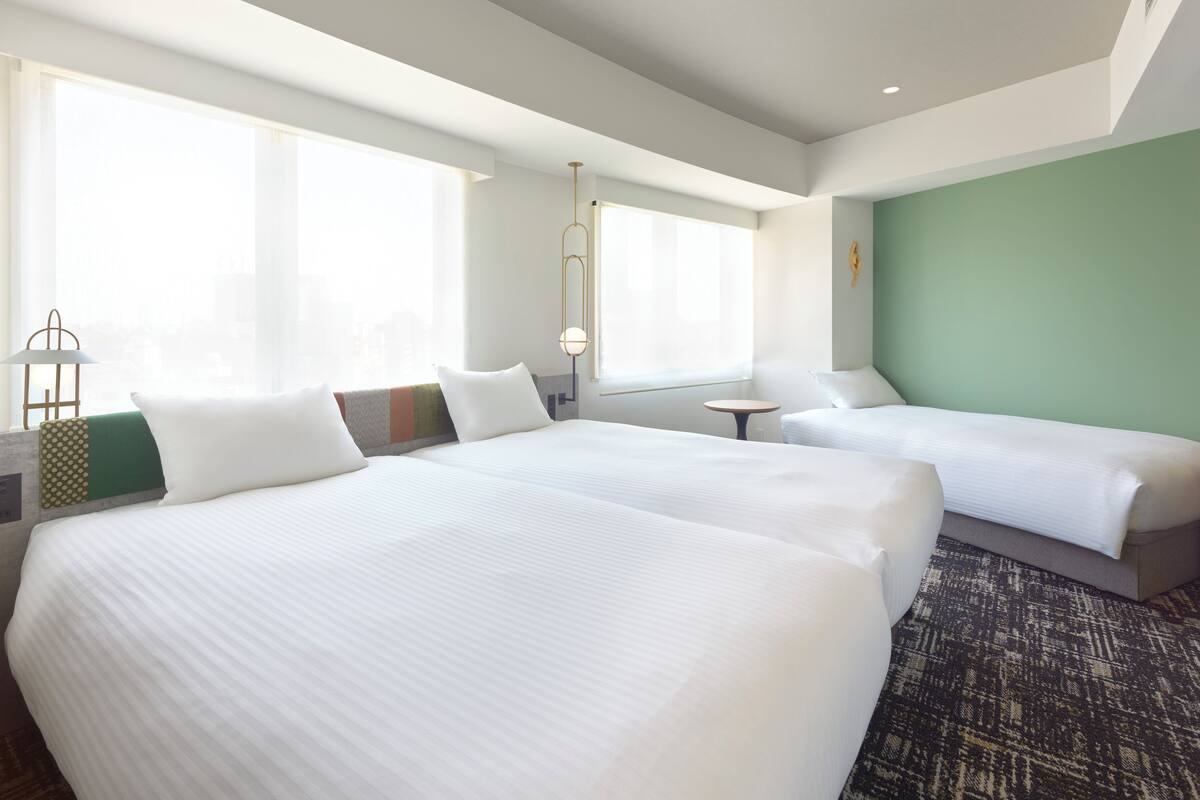 Quarto de hotel com duas camas, uma mesa pequena e vista da cidade através de amplas janelas.