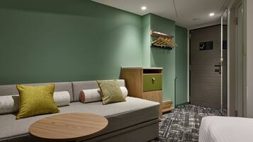 Una habitación de hotel moderna con un sofá gris, dos almohadones estampados, una mesa redonda de madera y una alfombra con diseño.