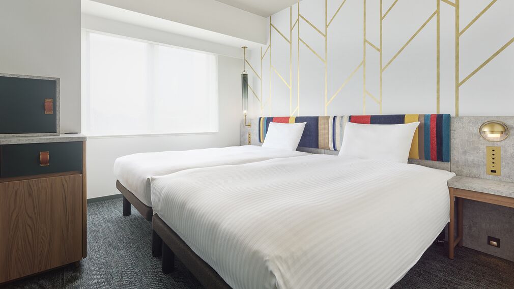 A hotel room with two beds, a desk, a television, and a large window.