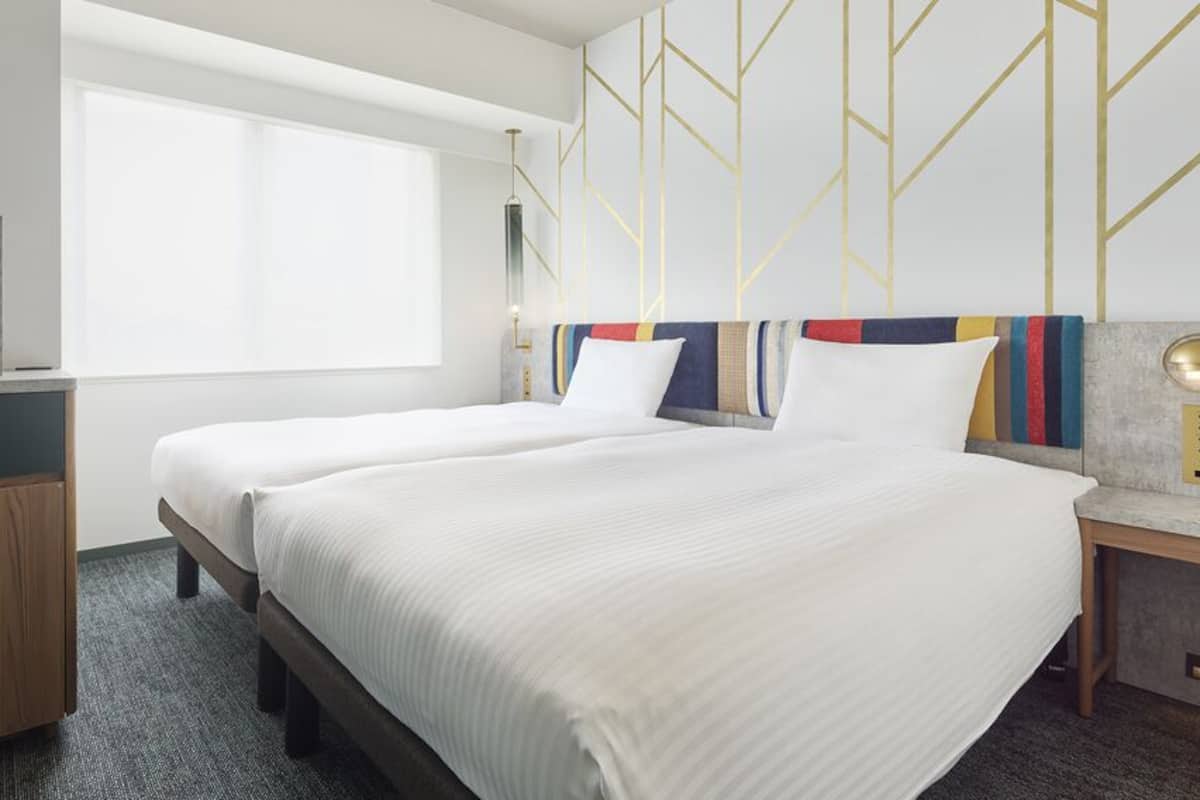 A hotel room with two beds, a desk, a television, and a large window.