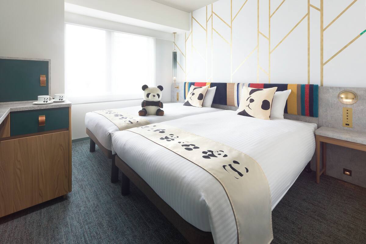 Quarto de hotel com uma cama grande, duas mesas de cabeceira, uma escrivaninha e uma janela.