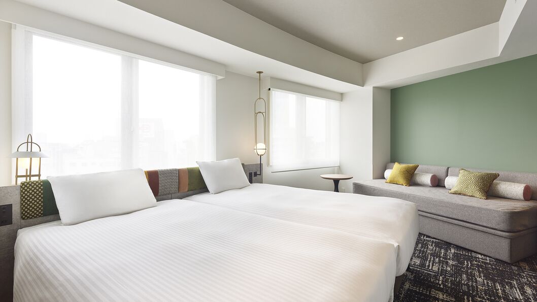 A hotel room with a large bed, a sofa, a small table, and a window.