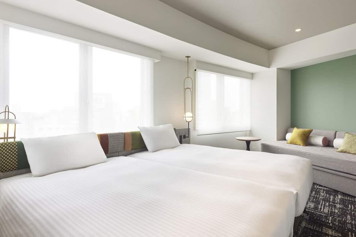 A hotel room with a large bed, a sofa, a small table, and a window.