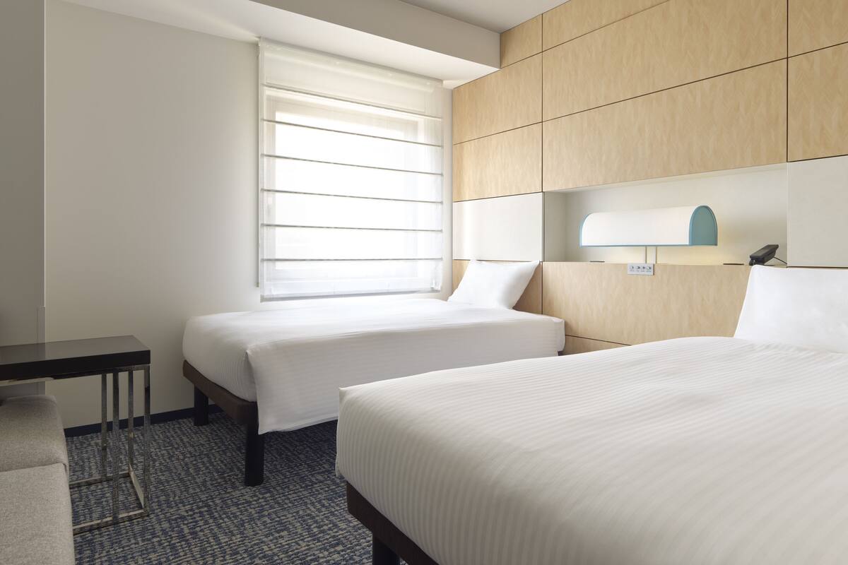 Quarto de hotel com duas camas, uma escrivaninha e uma janela com persianas.