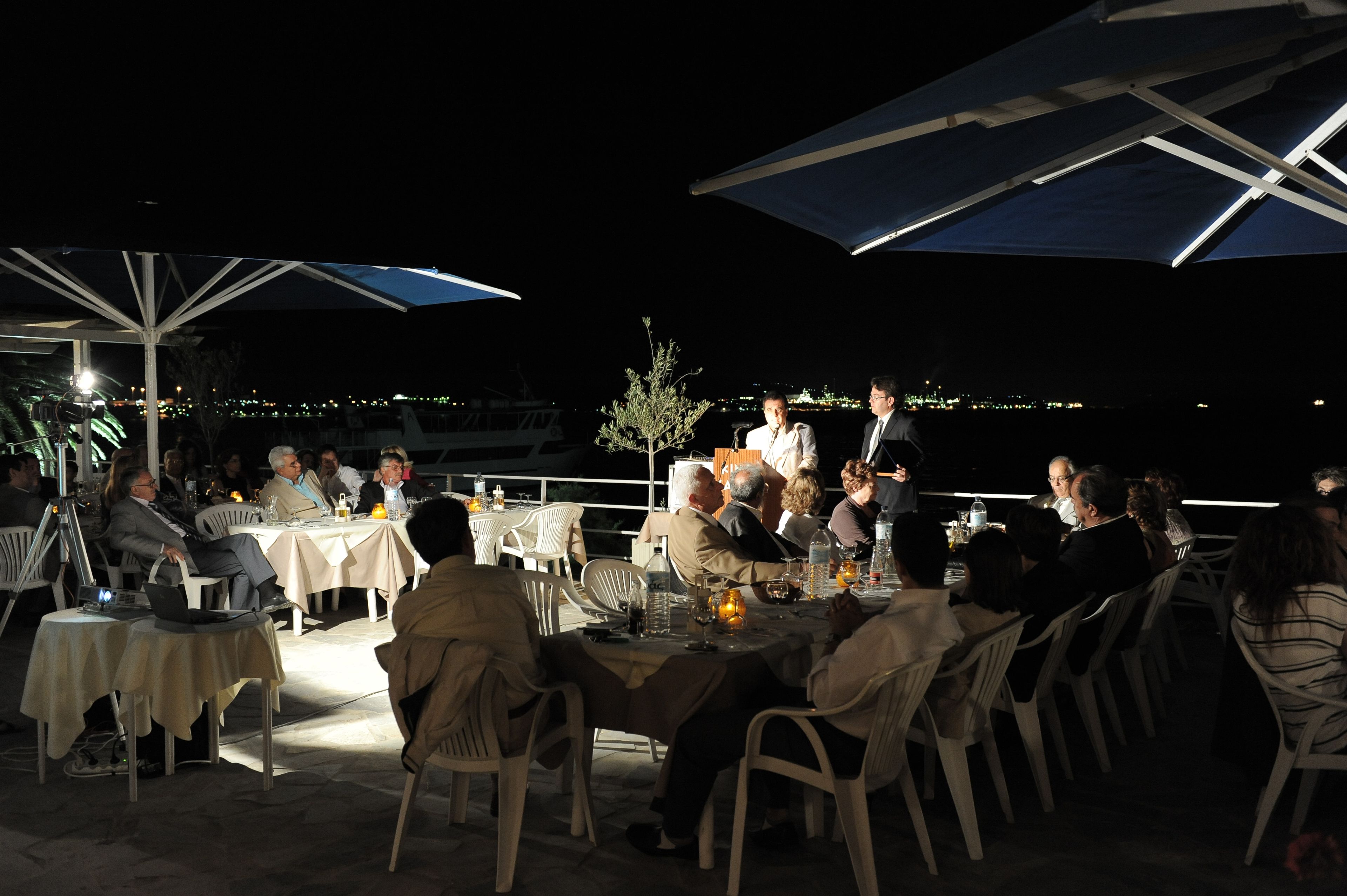 An outdoor dining area with tables and chairs, a speaker, and a view of the city at night.