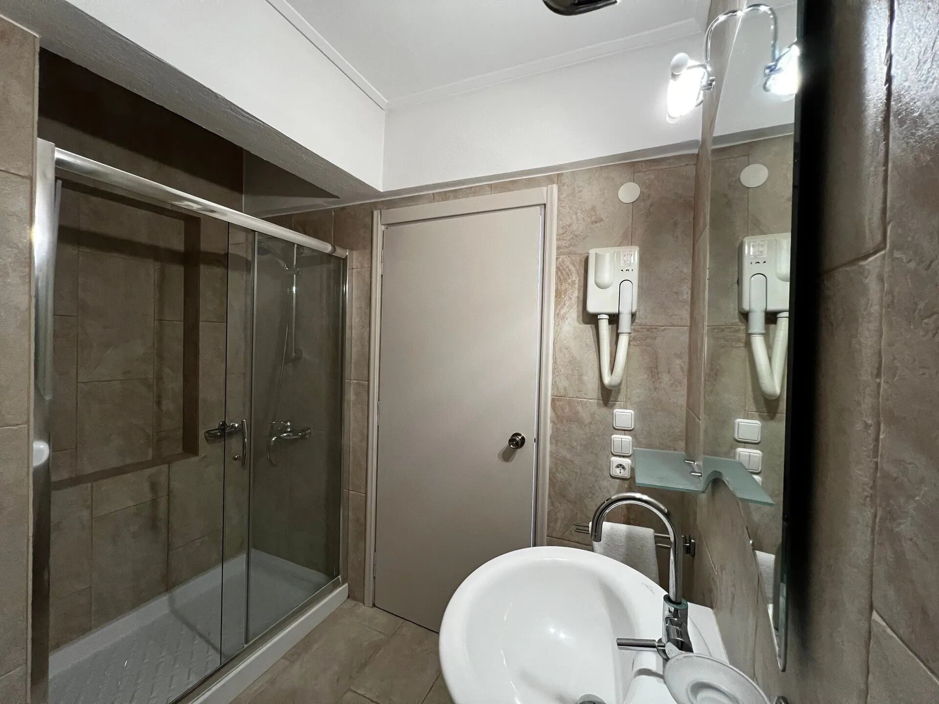 A bathroom with a glass-enclosed shower, a white sink, and a mirror with built-in lighting.