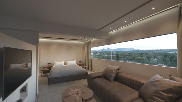 Una habitación de hotel moderna con una cama grande, un sofá, una mesita redonda y un ventanal con vistas a la ciudad.