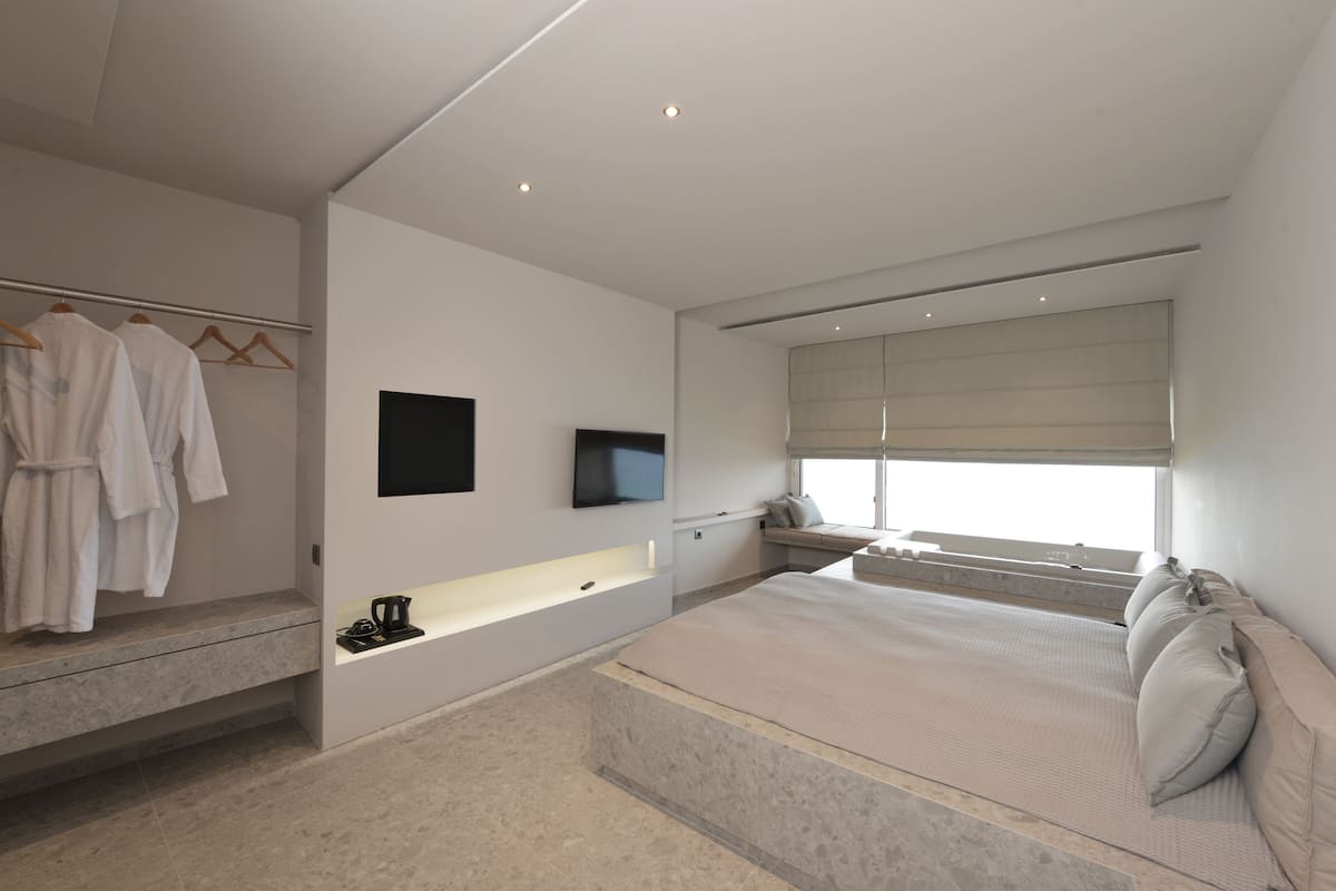 Un dormitorio moderno con una cama grande, una bañera integrada y un televisor de pantalla plana.