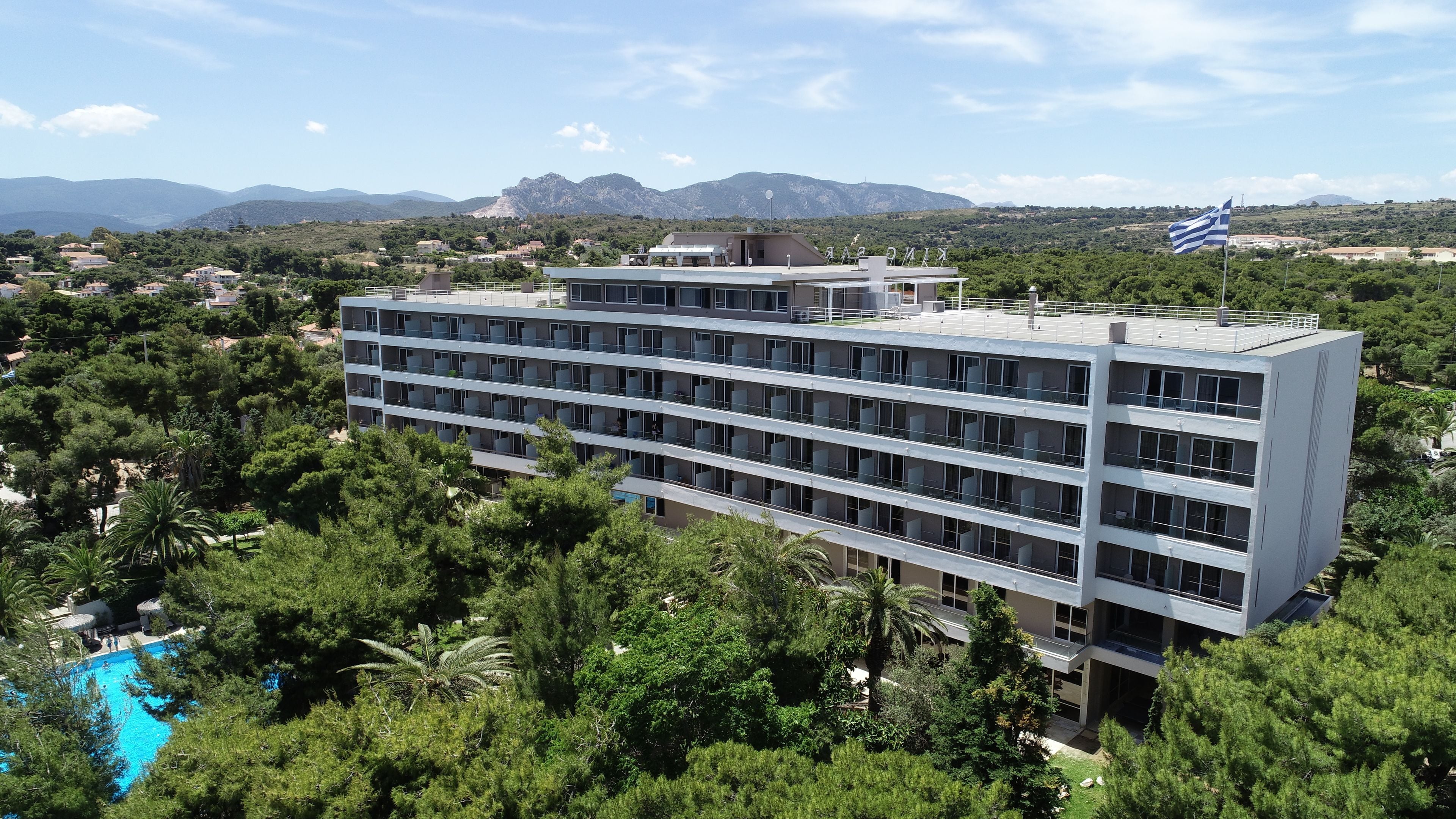 Ein mehrstöckiges Hotel mit flachem Dach, umgeben von üppiger Vegetation und freiem Blick auf entfernte Berge.