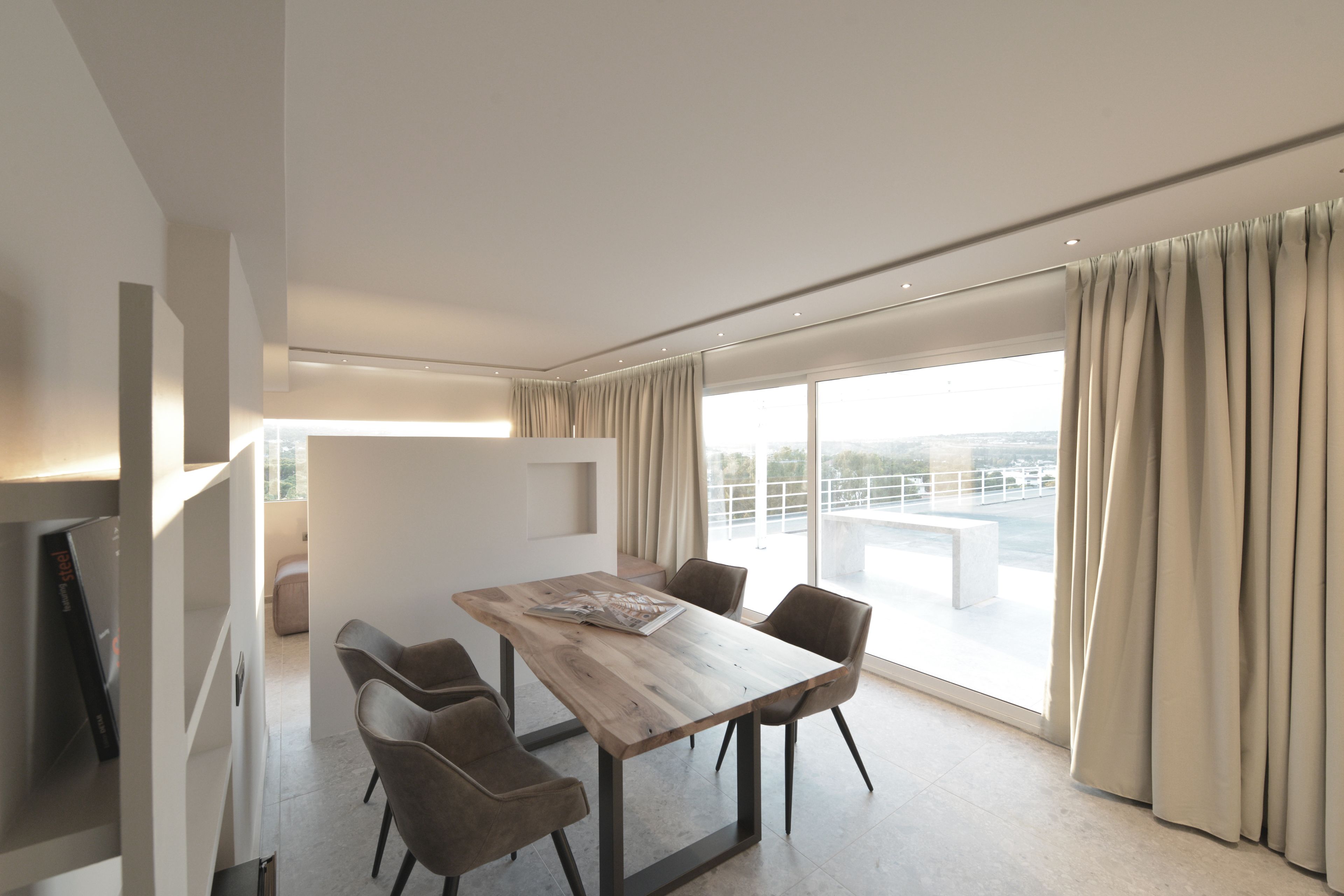 Een moderne eetruimte met een houten tafel en stoelen, grote ramen met gordijnen en uitzicht op de stad.