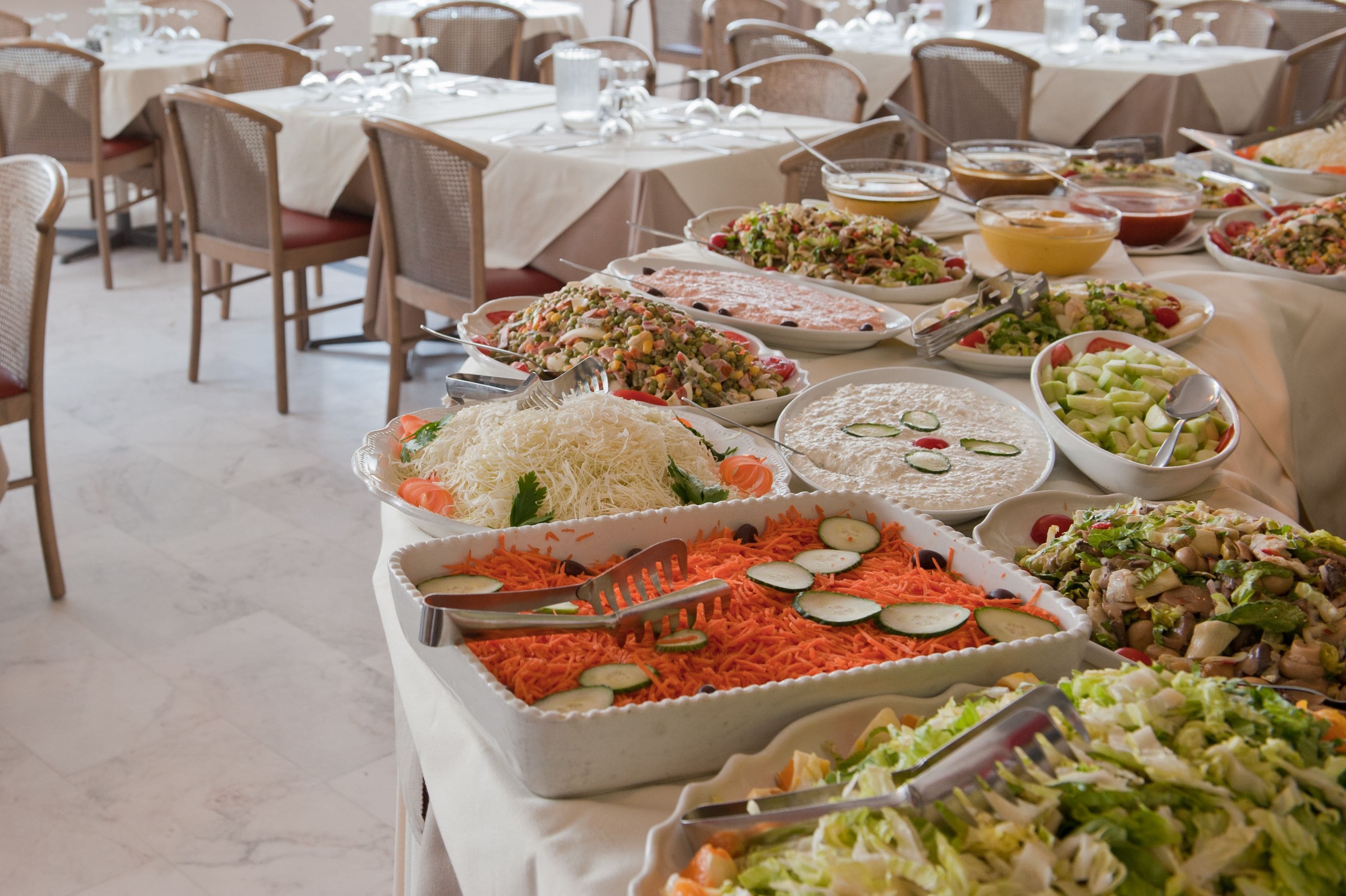 A buffet setup with various dishes, including salads, pasta, and rice, arranged on tables in a dining area.