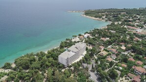 Vista aérea de una zona costera con un edificio grande, probablemente un hotel, junto a una playa de aguas turquesas y cristalinas.