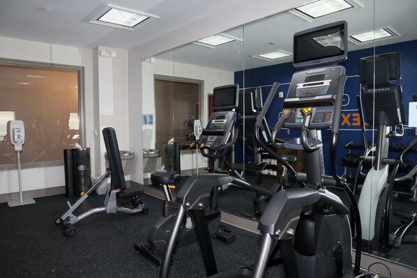 Et fitnesscenter med forskellig træningsudstyr, herunder løbebånd og styrkemaskiner, samt et stort spejl der afspejler rummet.