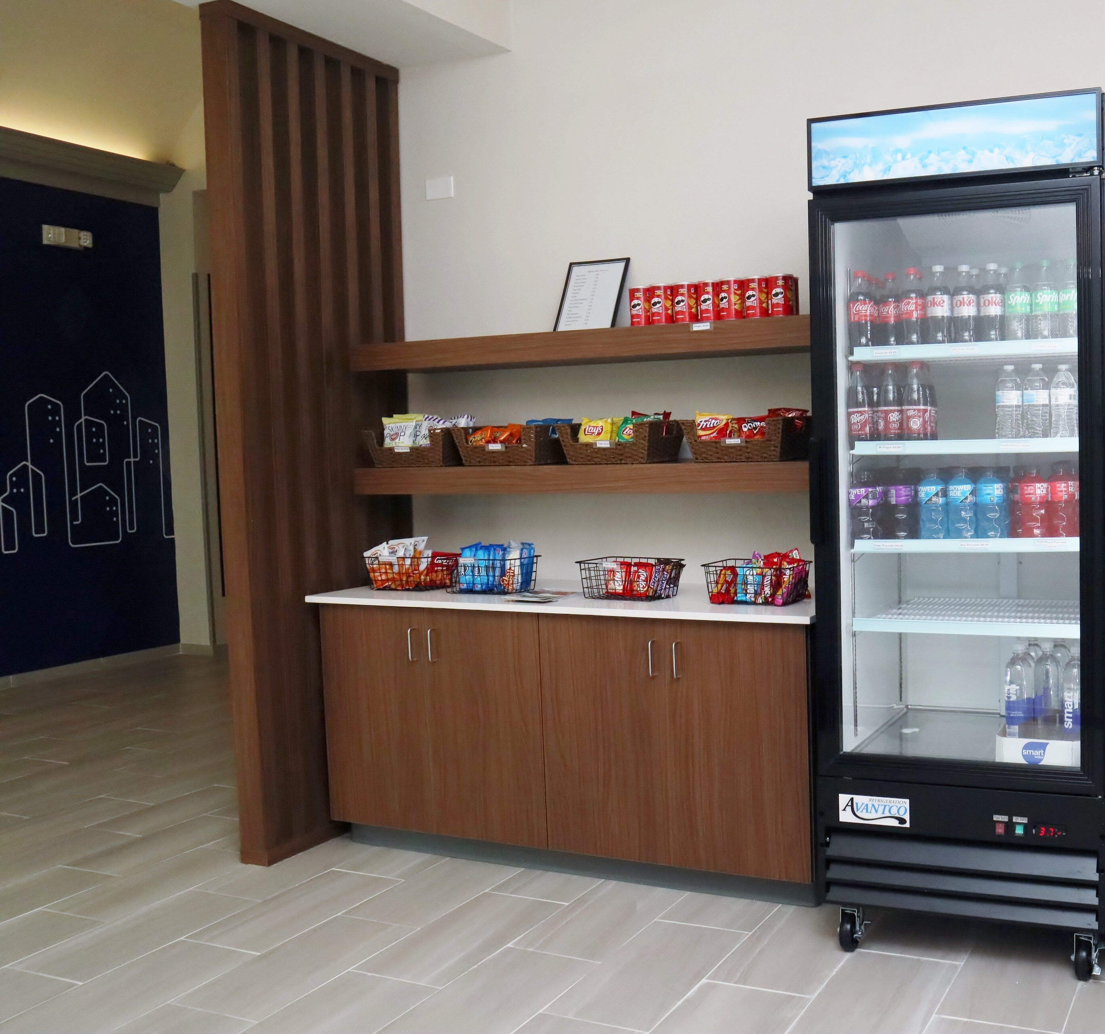 Een automaat vol drankjes en snacks, een houten kast met manden voor snacks, en een deur met een stadsgezichtsmural.