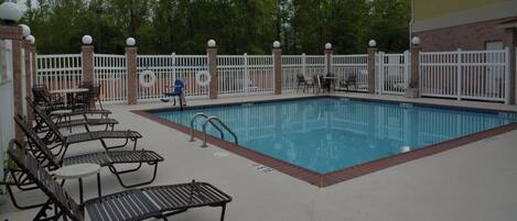 A swimming pool with a white fence, lounge chairs, and a brick wall.
