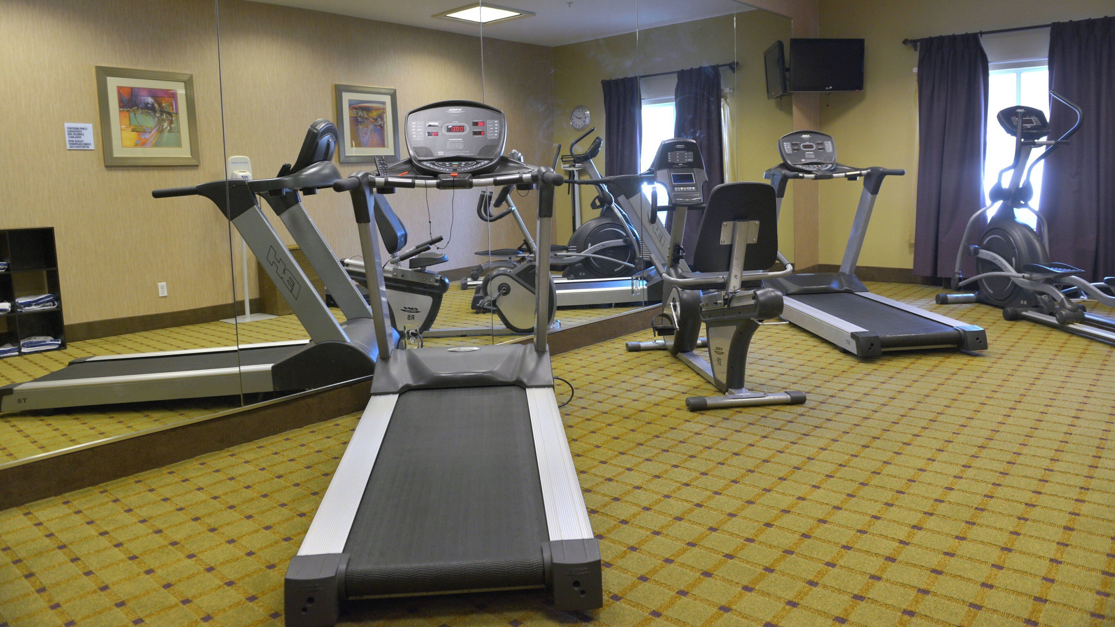 Ein Fitnessraum eines Hotels mit mehreren Trainingsgeräten, darunter Laufbändern und Ergometer, sowie einer Spiegelwand.