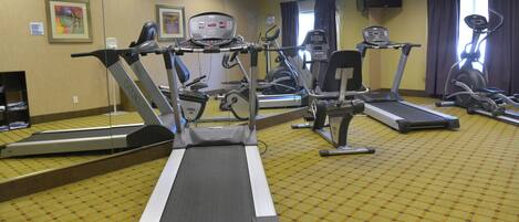 A hotel fitness center with multiple exercise machines, including treadmills and stationary bikes, and a mirrored wall.