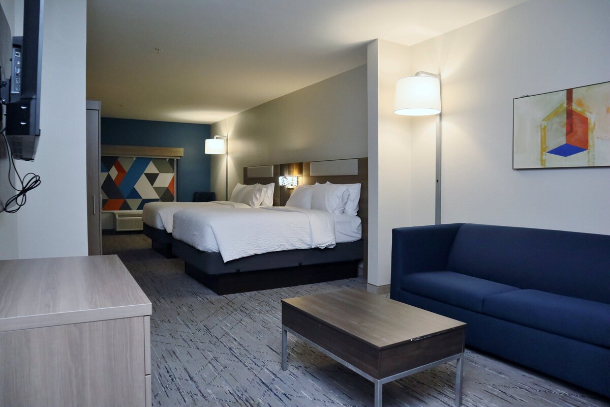 A hotel room with a bed, a blue sofa, a wooden coffee table, and a painting on the wall.