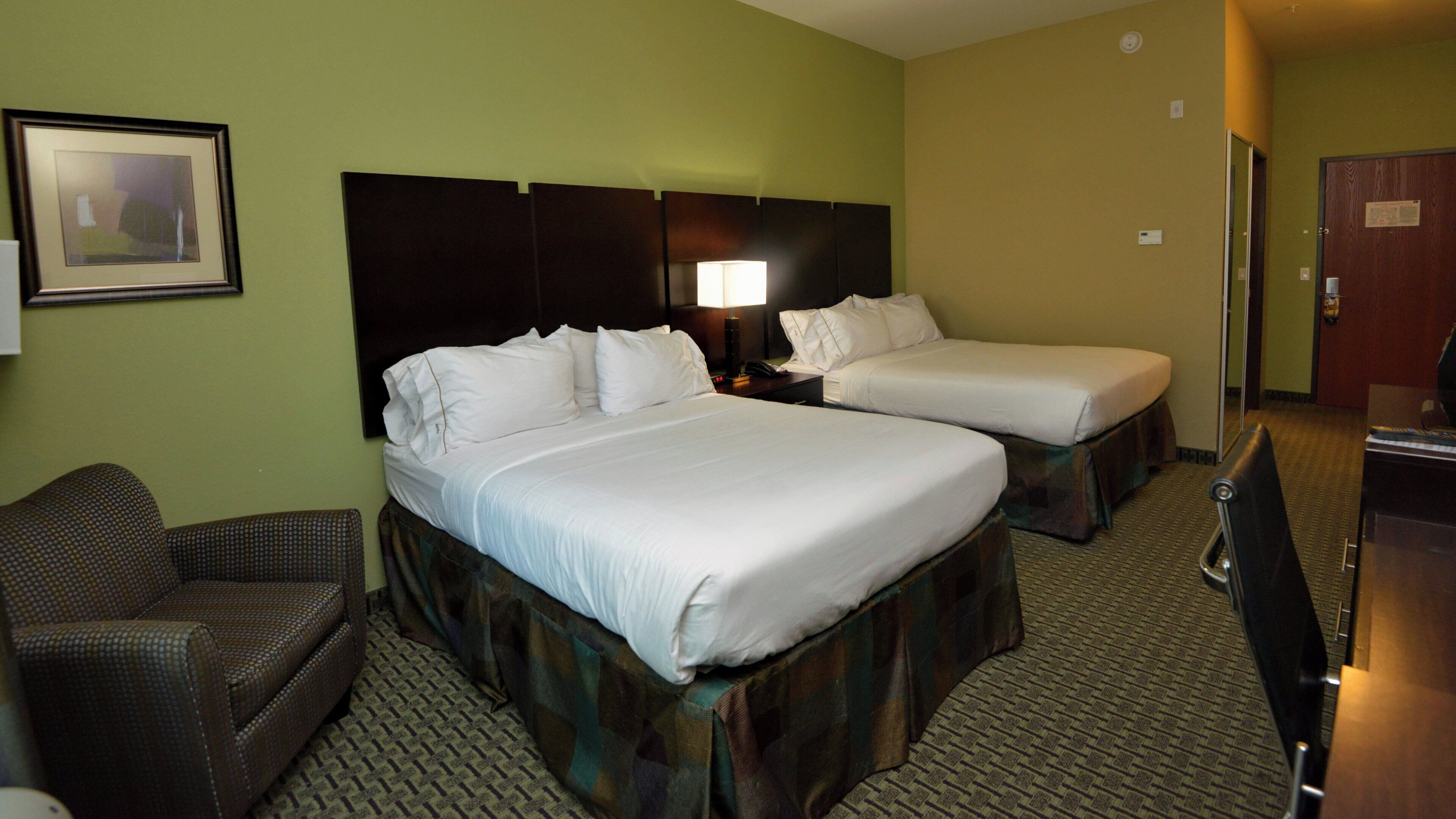 A hotel room with two beds, a chair, a desk, and a lamp.