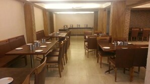 A restaurant with multiple wooden tables and chairs, a central counter, and a tiled floor. - Hotel Sunny International (Mahabaleshwar)
