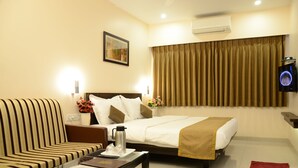 A hotel room with a bed, a sofa, a coffee table, and a TV. - Hotel Sunny International (Mahabaleshwar)