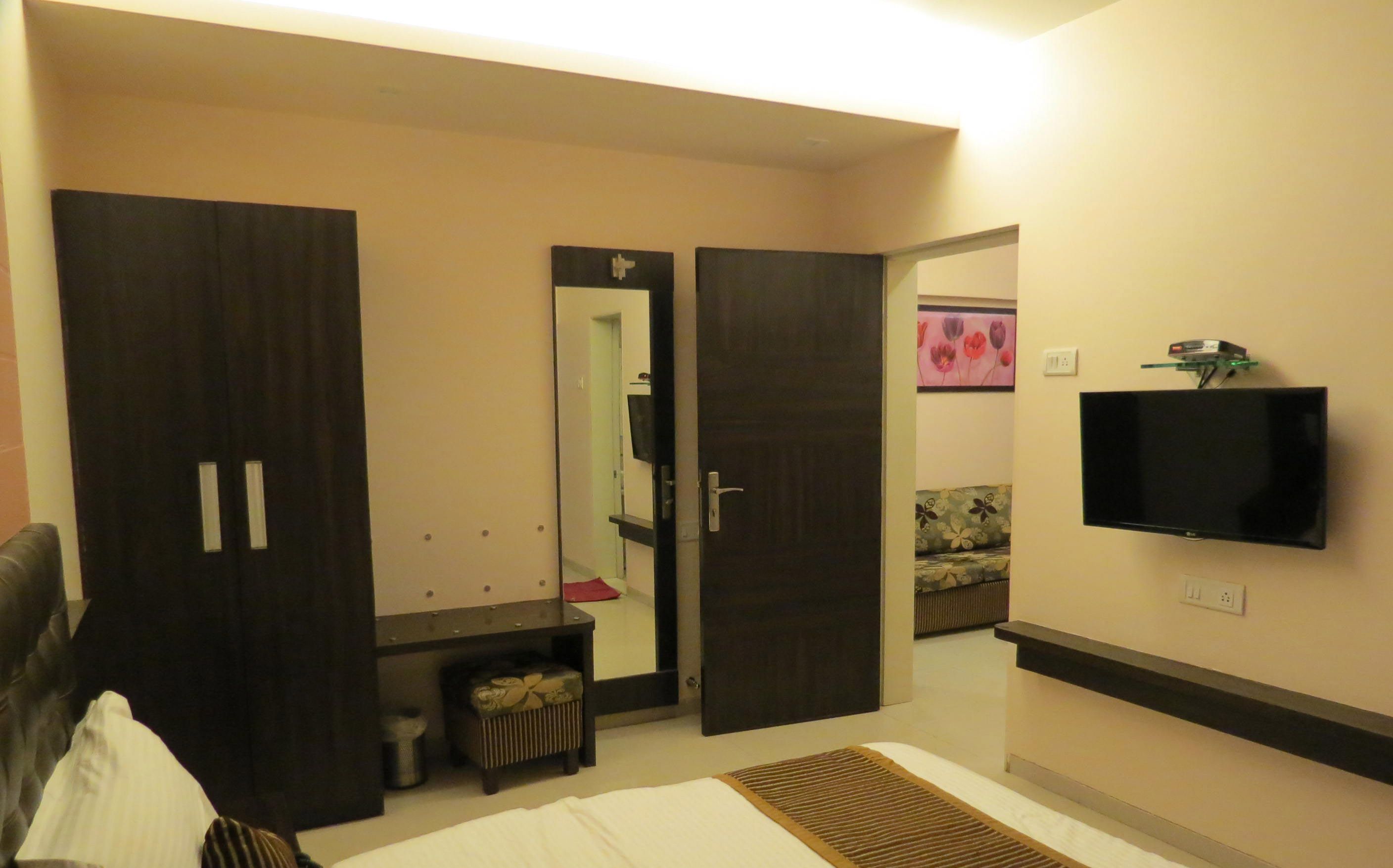 A hotel room with a bed, a TV mounted on the wall, a wardrobe, and a mirror.