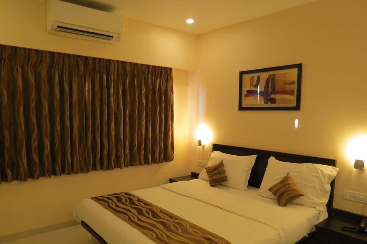 A hotel room with a bed, curtains, a painting, and wall-mounted lights.