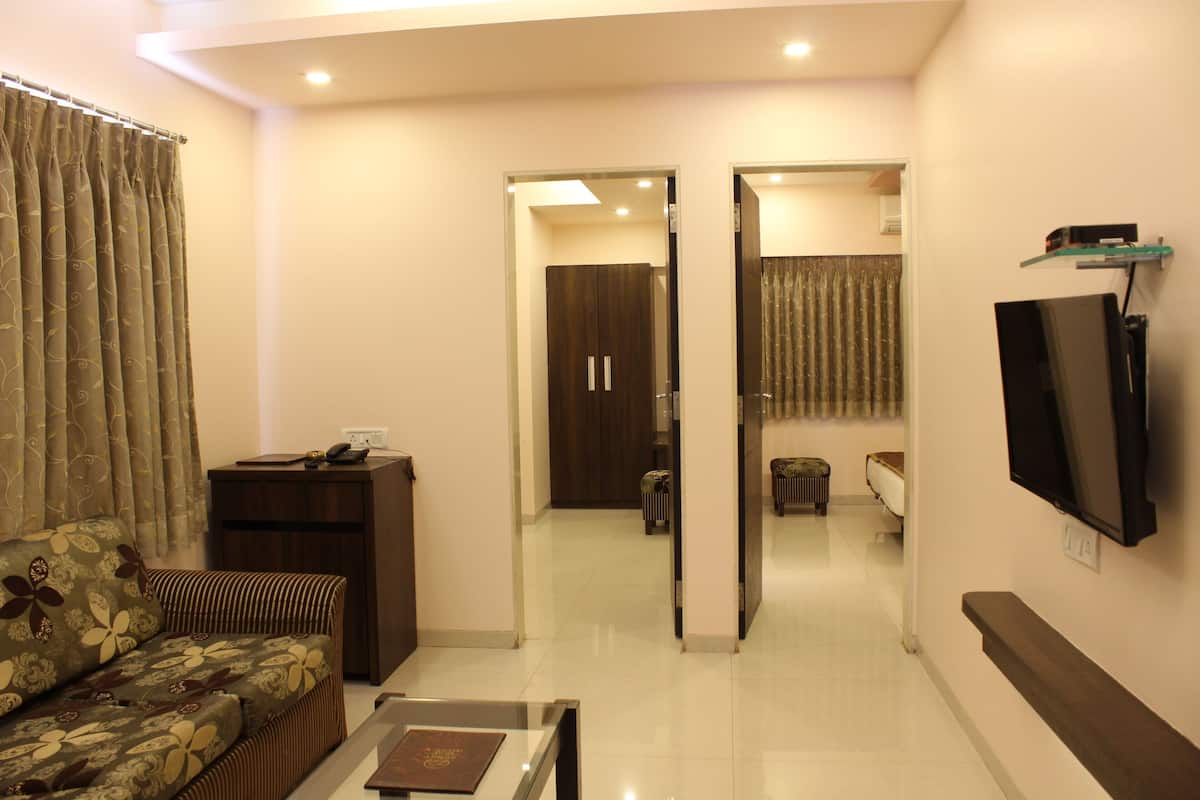 A living room with a sofa, a coffee table, a TV mounted on the wall, and a door leading to another room.
