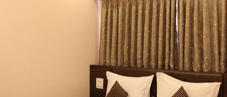 A neatly made bed with a white and brown striped bedspread, a ceiling fan, and a window with patterned curtains.