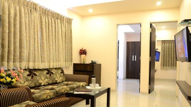 A living room with a sofa, a coffee table, and a television. - Hotel Sunny International (Mahabaleshwar)