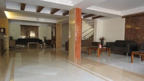 A spacious lobby with a polished marble floor, a staircase, and a reception area with a sofa and a coffee table. - Hotel Sunny International (Mahabaleshwar)