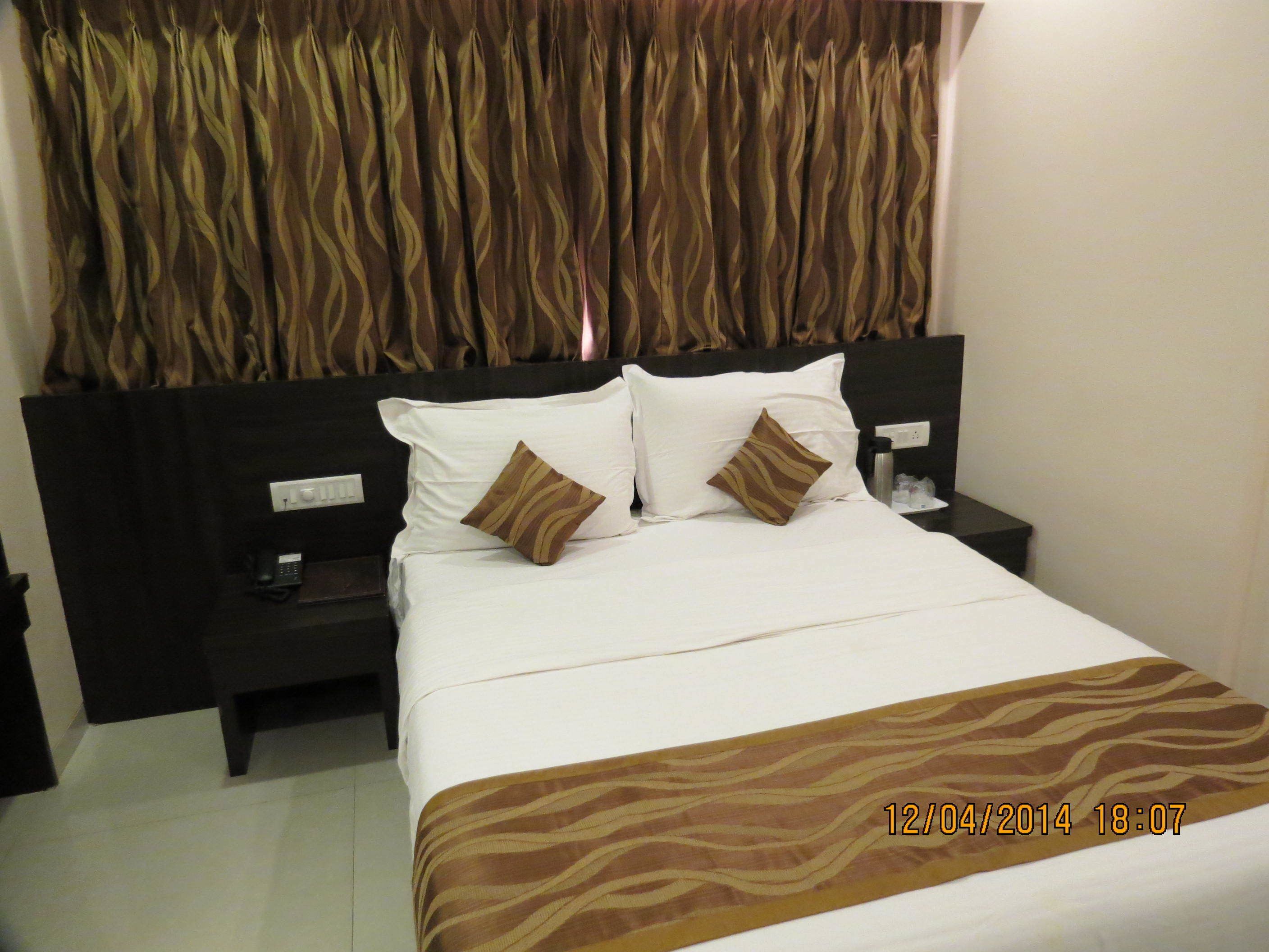 A hotel room with a bed, two pillows, a nightstand, a telephone, and a wall with a curtain.