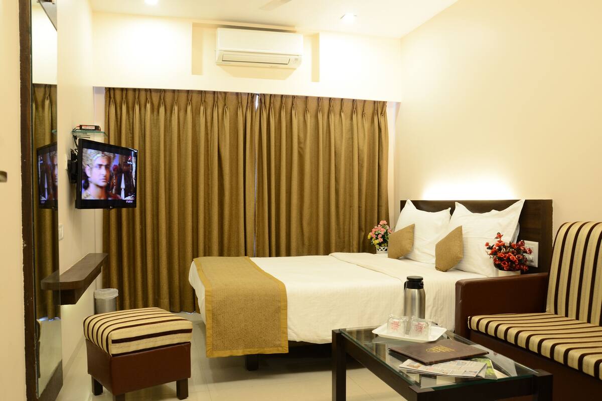 A hotel room with a bed, a TV, a sofa, a coffee table, and a small table with a vase of flowers.