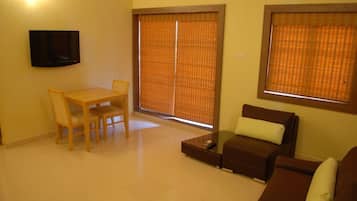 A living room with a TV, a dining table with chairs, a sofa, and a window with blinds.