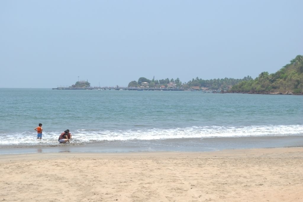 Una playa con una vista despejada del mar y una costa distante con edificios y árboles.